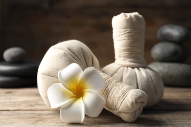 Photo of Herbal bags, spa stones and plumeria flower on wooden table, closeup