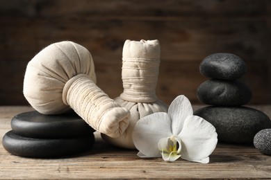 Photo of Herbal bags, spa stones and orchid flower on wooden table, closeup