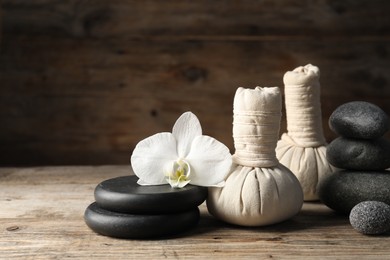 Photo of Herbal bags, spa stones and orchid flower on wooden table. Space for text