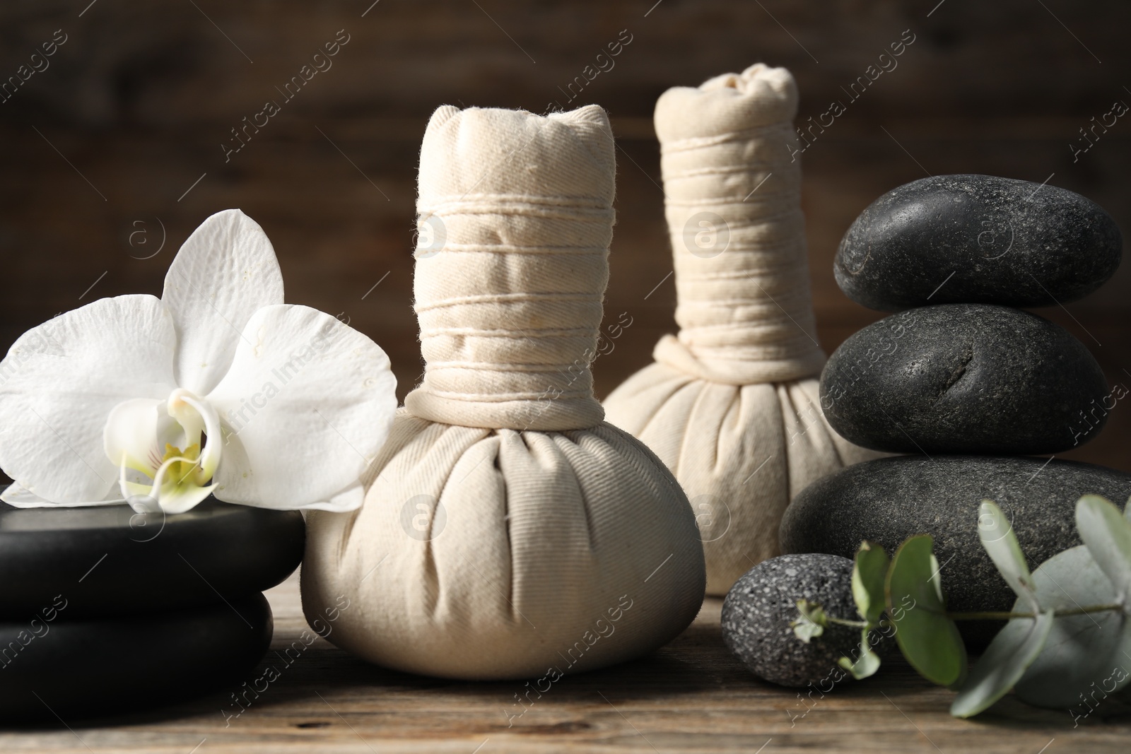 Photo of Composition with herbal bags and spa stones on wooden table, closeup