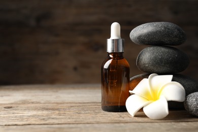 Photo of Spa stones, cosmetic product and plumeria flower on wooden table, closeup. Space for text