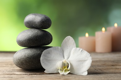 Photo of Spa stones and orchid flower on wooden table, closeup
