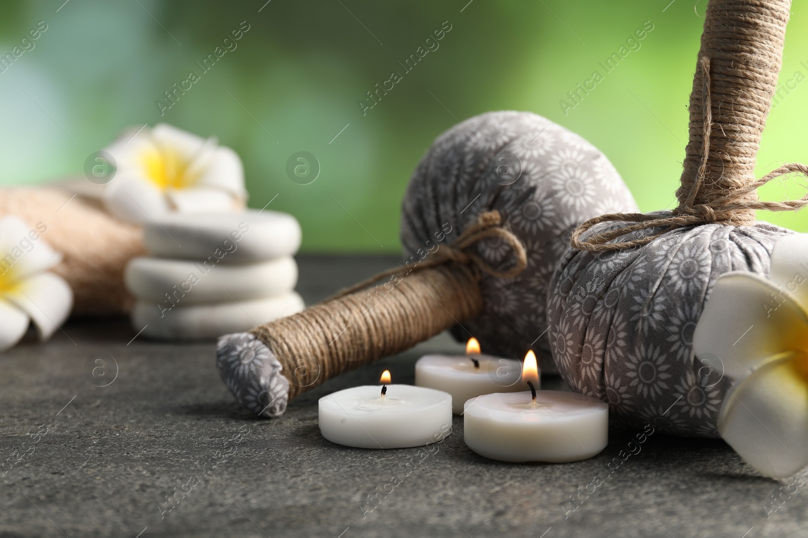 Herbal bags, spa stones, plumeria flowers and burning candles on grey table, closeup Photo of Herbal bags, spa stones, plumeria flowers and burning candles on grey table, closeup