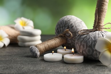 Photo of Herbal bags, spa stones, plumeria flowers and burning candles on grey table, closeup
