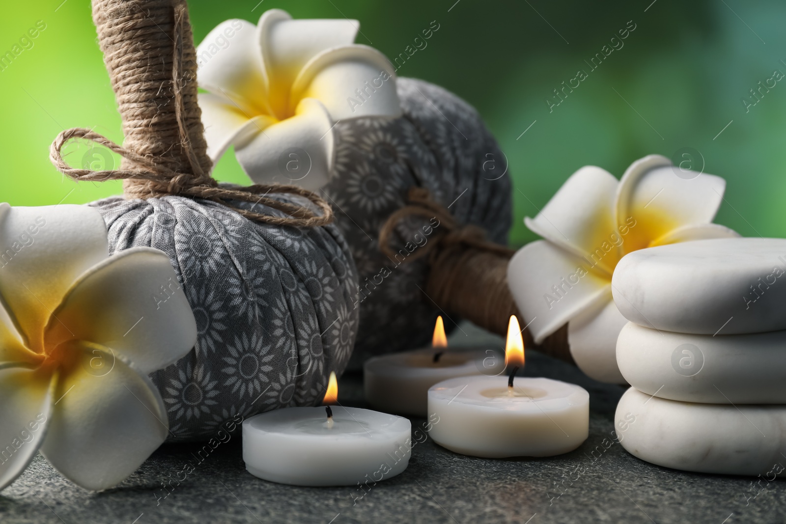 Herbal bags, spa stones, plumeria flowers and burning candles on grey table, closeup Photo of Herbal bags, spa stones, plumeria flowers and burning candles on grey table, closeup