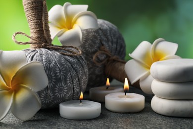 Photo of Herbal bags, spa stones, plumeria flowers and burning candles on grey table, closeup