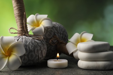 Photo of Herbal bags, spa stones, plumeria flowers and burning candle on grey table, closeup