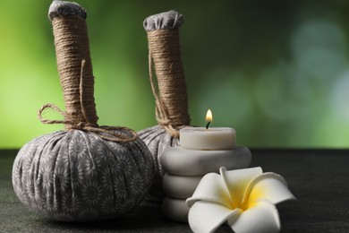 Photo of Herbal bags, spa stones, plumeria flower and burning candle on grey table, closeup