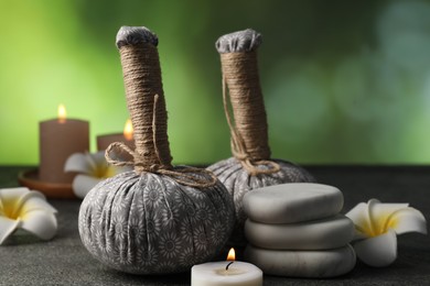 Photo of Herbal bags, spa stones, plumeria flowers and burning candles on grey table, closeup