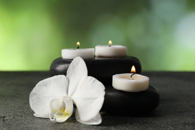 Photo of Spa stones, burning candles and orchid flower on grey table, closeup