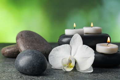 Photo of Spa stones, burning candles and orchid flower on grey table, closeup