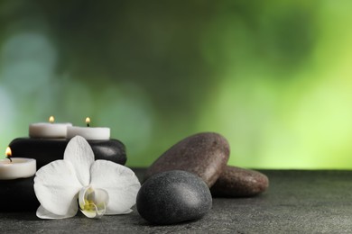 Photo of Spa stones, burning candles and orchid flower on grey table, closeup. Space for text