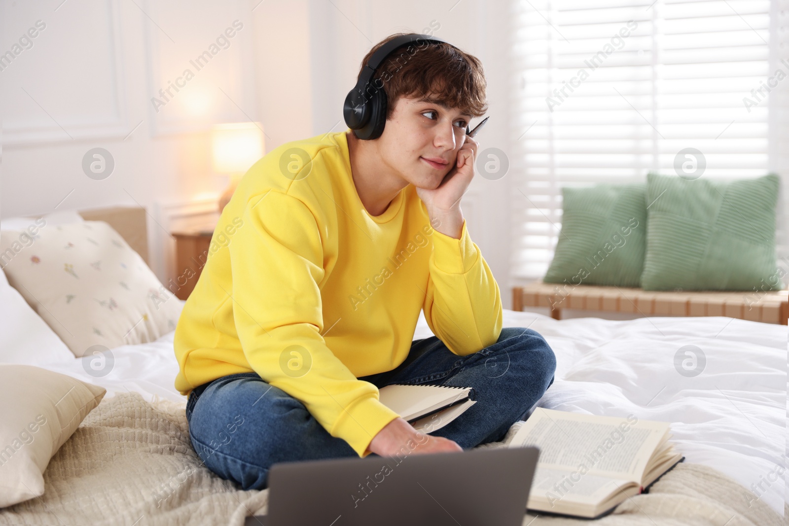 Teenage student in headphones studying on bed at home Photo of Teenage student in headphones studying on bed at home