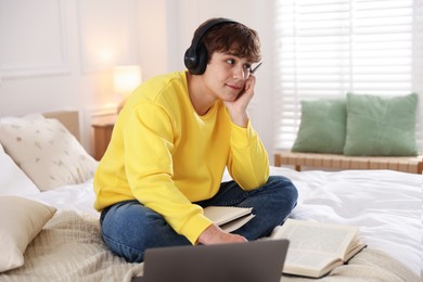 Photo of Teenage student in headphones studying on bed at home