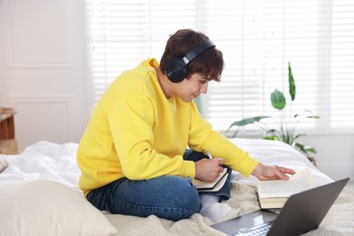 Photo of Teenage student in headphones studying on bed at home