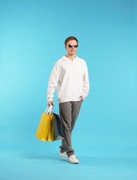 Photo of Cheerful man with shopping bags on light blue background