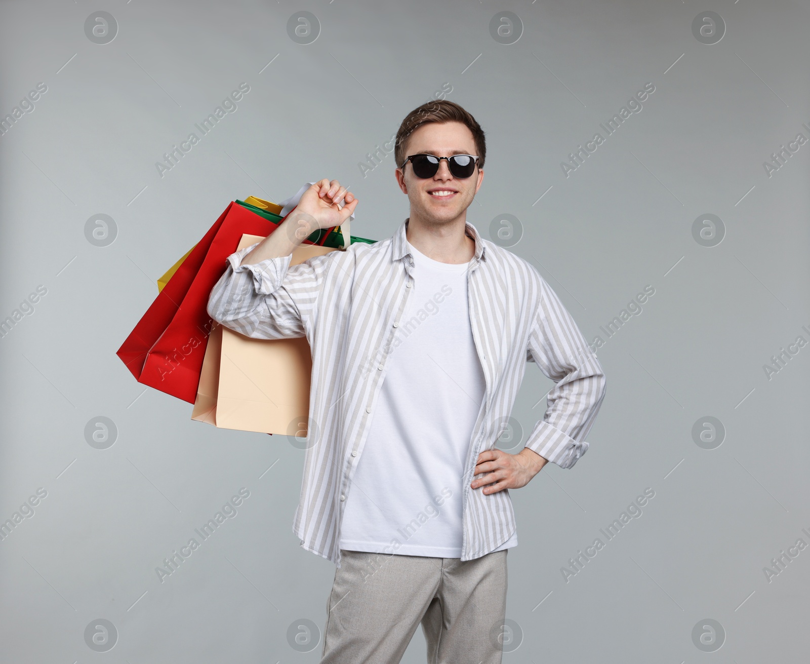 Cheerful man with shopping bags on light grey background Photo of Cheerful man with shopping bags on light grey background