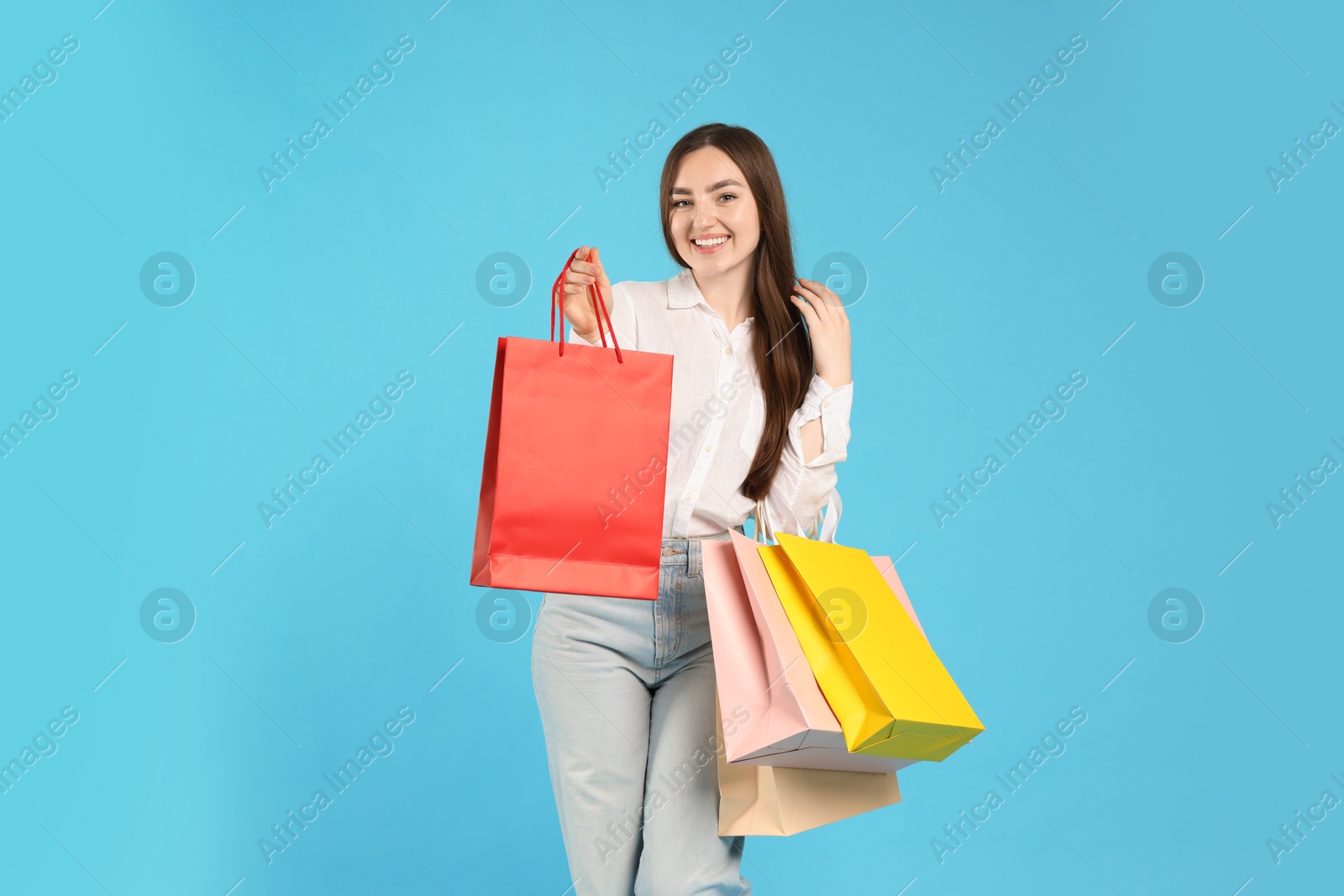 Positive woman with shopping bags on light blue background Photo of Positive woman with shopping bags on light blue background