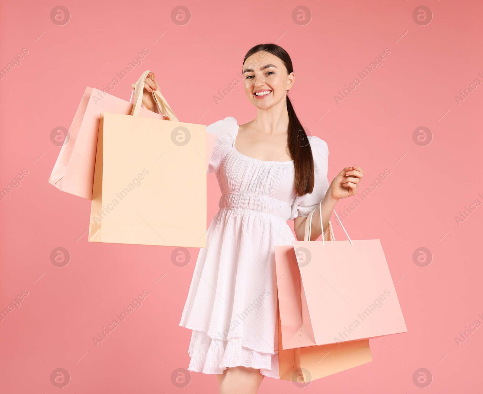 Positive woman with shopping bags on light pink background Photo of Positive woman with shopping bags on light pink background