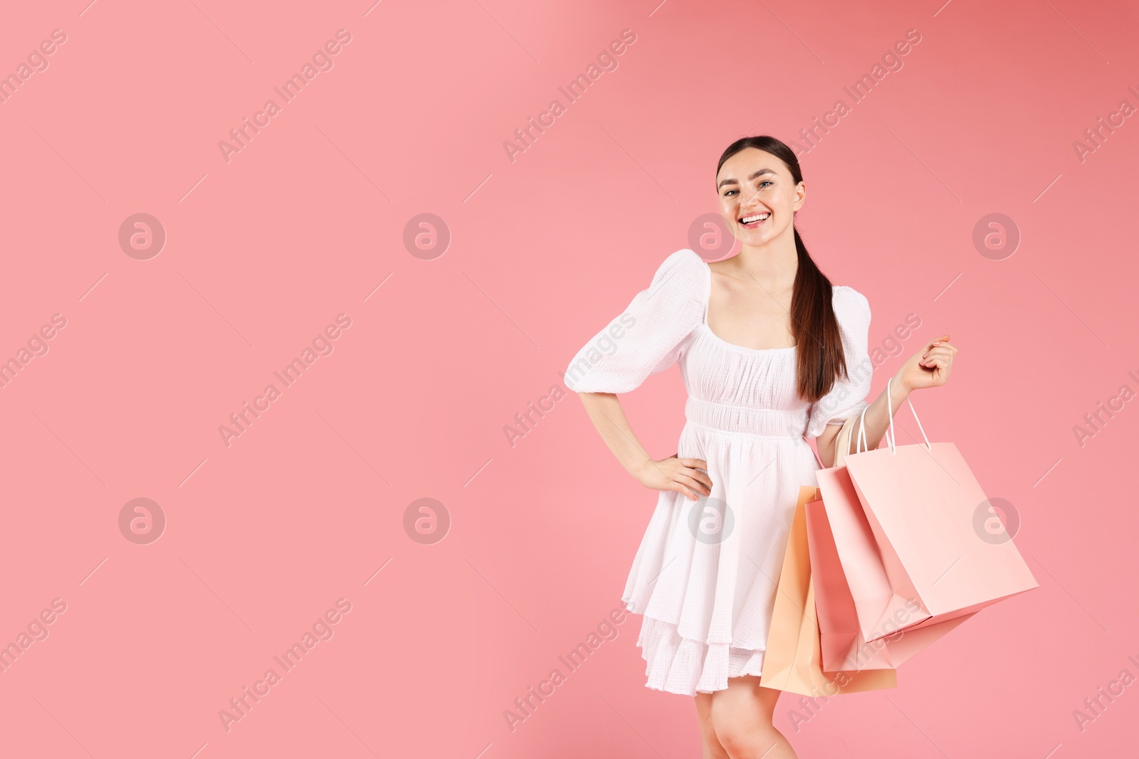 Positive woman with shopping bags on light pink background. Space for text Photo of Positive woman with shopping bags on light pink background. Space for text