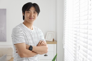 Photo of Portrait of handsome Asian man with crossed arms at home. Space for text