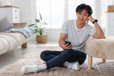 Photo of Handsome Asian man with smartphone on floor at home