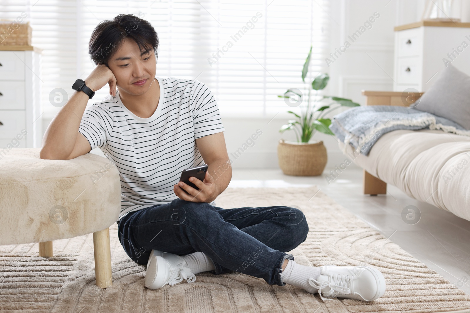 Handsome Asian man with smartphone on floor at home Photo of Handsome Asian man with smartphone on floor at home