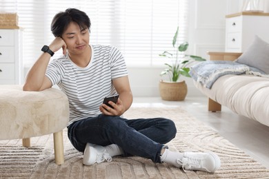Photo of Handsome Asian man with smartphone on floor at home