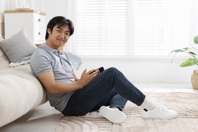 Photo of Handsome Asian man with smartphone on floor at home