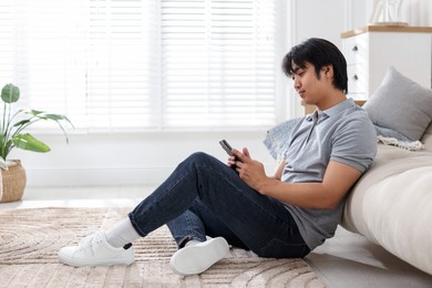Photo of Handsome Asian man with smartphone on floor at home