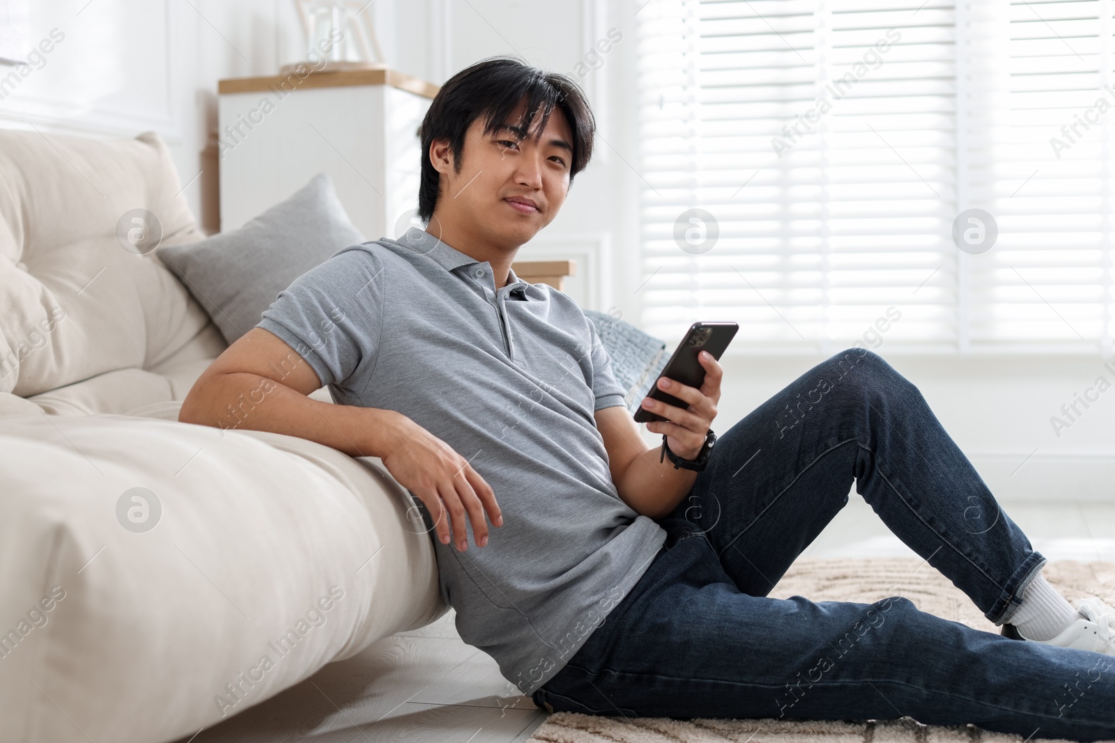 Handsome Asian man with smartphone on floor at home Photo of Handsome Asian man with smartphone on floor at home