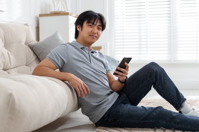 Photo of Handsome Asian man with smartphone on floor at home
