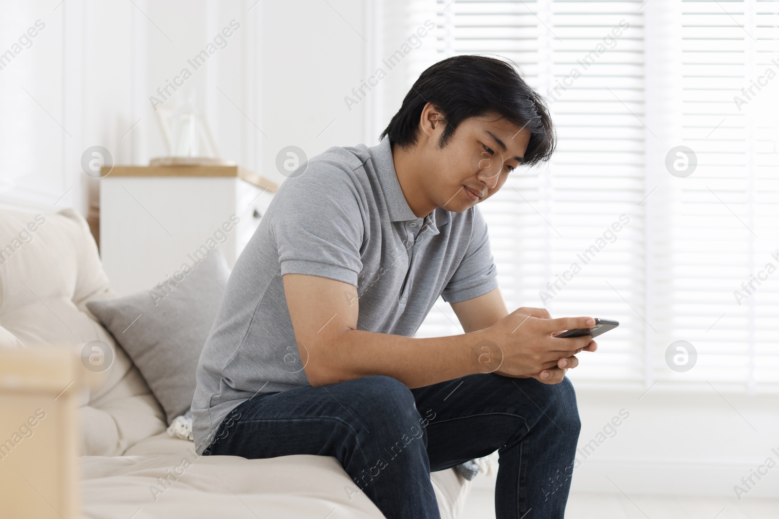 Handsome Asian man with smartphone on sofa at home Photo of Handsome Asian man with smartphone on sofa at home