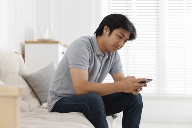 Photo of Handsome Asian man with smartphone on sofa at home