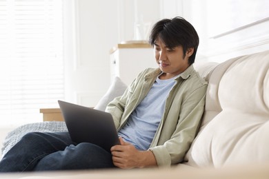 Photo of Handsome Asian man with laptop on sofa at home