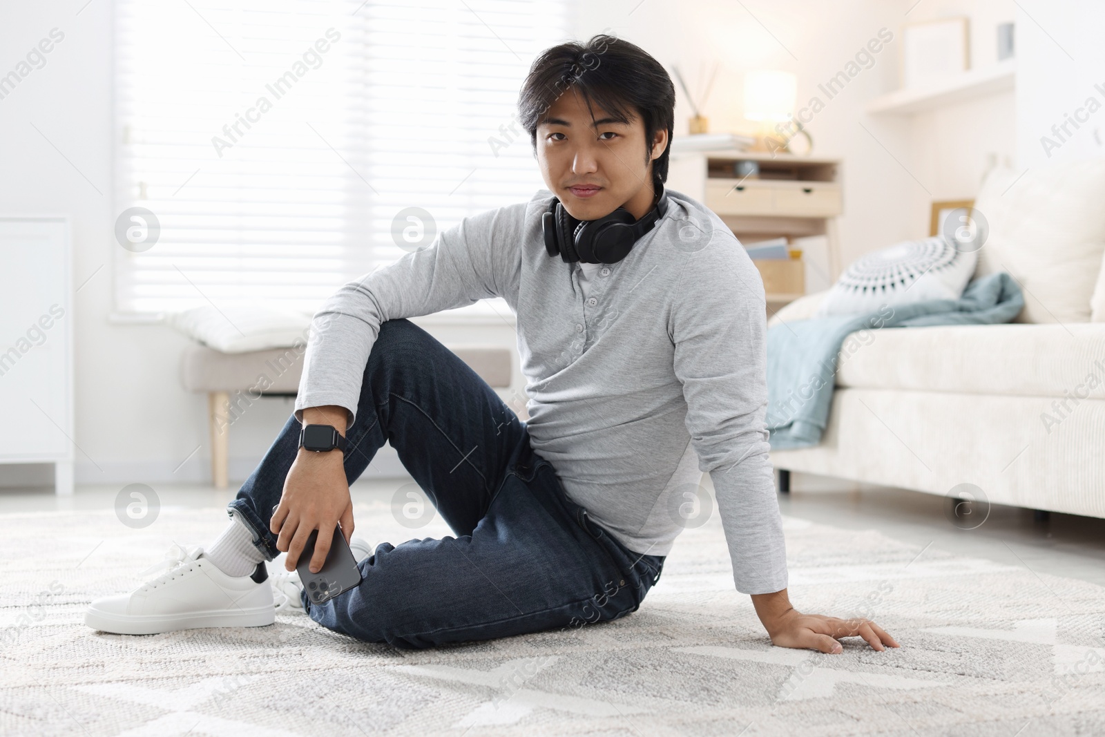 Handsome Asian man with headphones and smartphone on floor at home Photo of Handsome Asian man with headphones and smartphone on floor at home