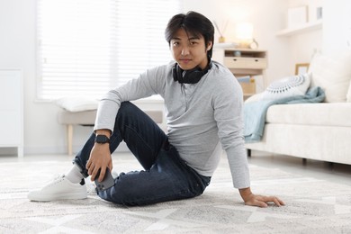 Photo of Handsome Asian man with headphones and smartphone on floor at home