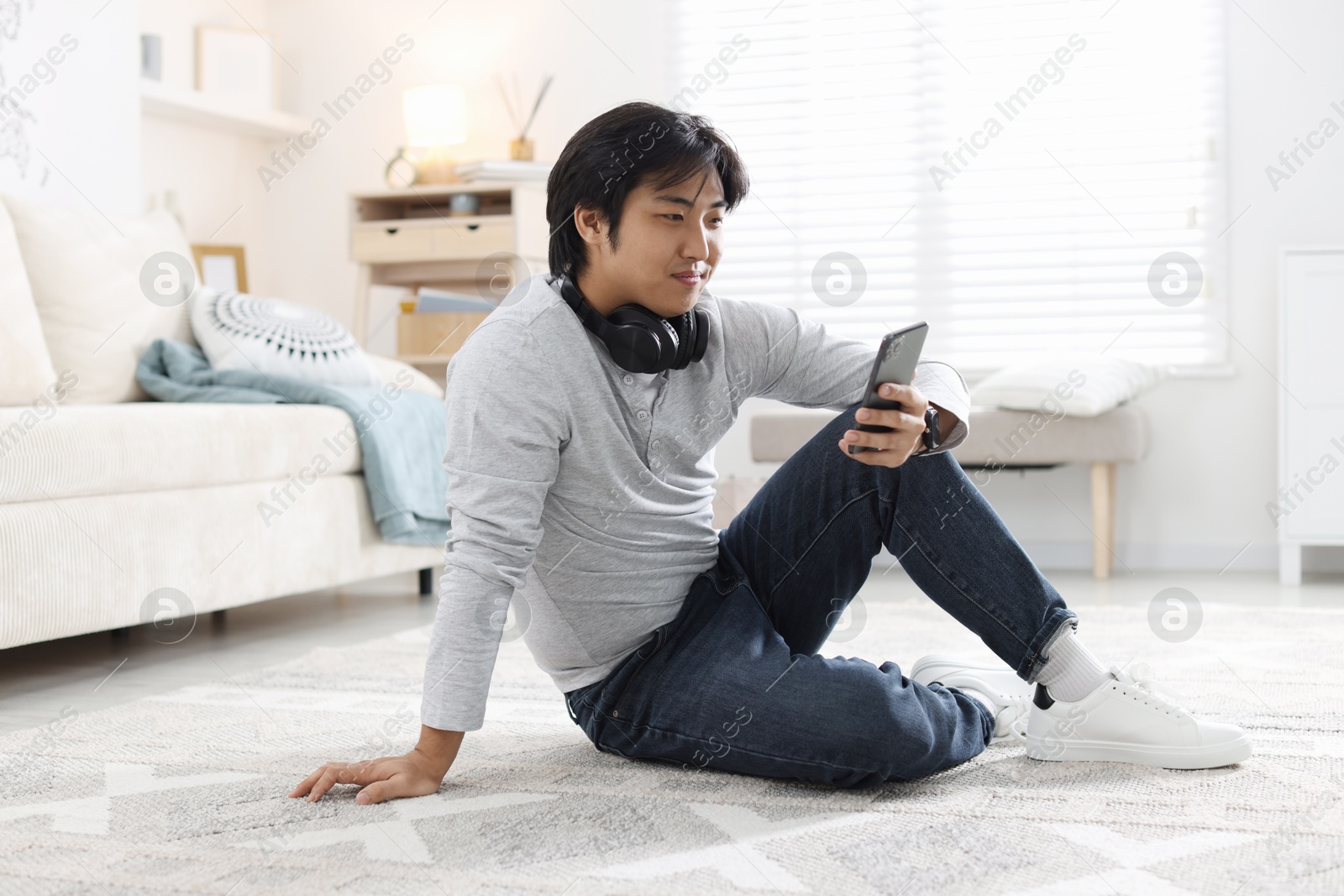 Handsome Asian man with headphones and smartphone on floor at home Photo of Handsome Asian man with headphones and smartphone on floor at home
