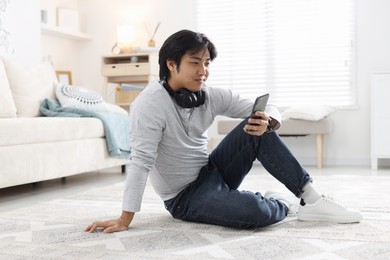 Photo of Handsome Asian man with headphones and smartphone on floor at home
