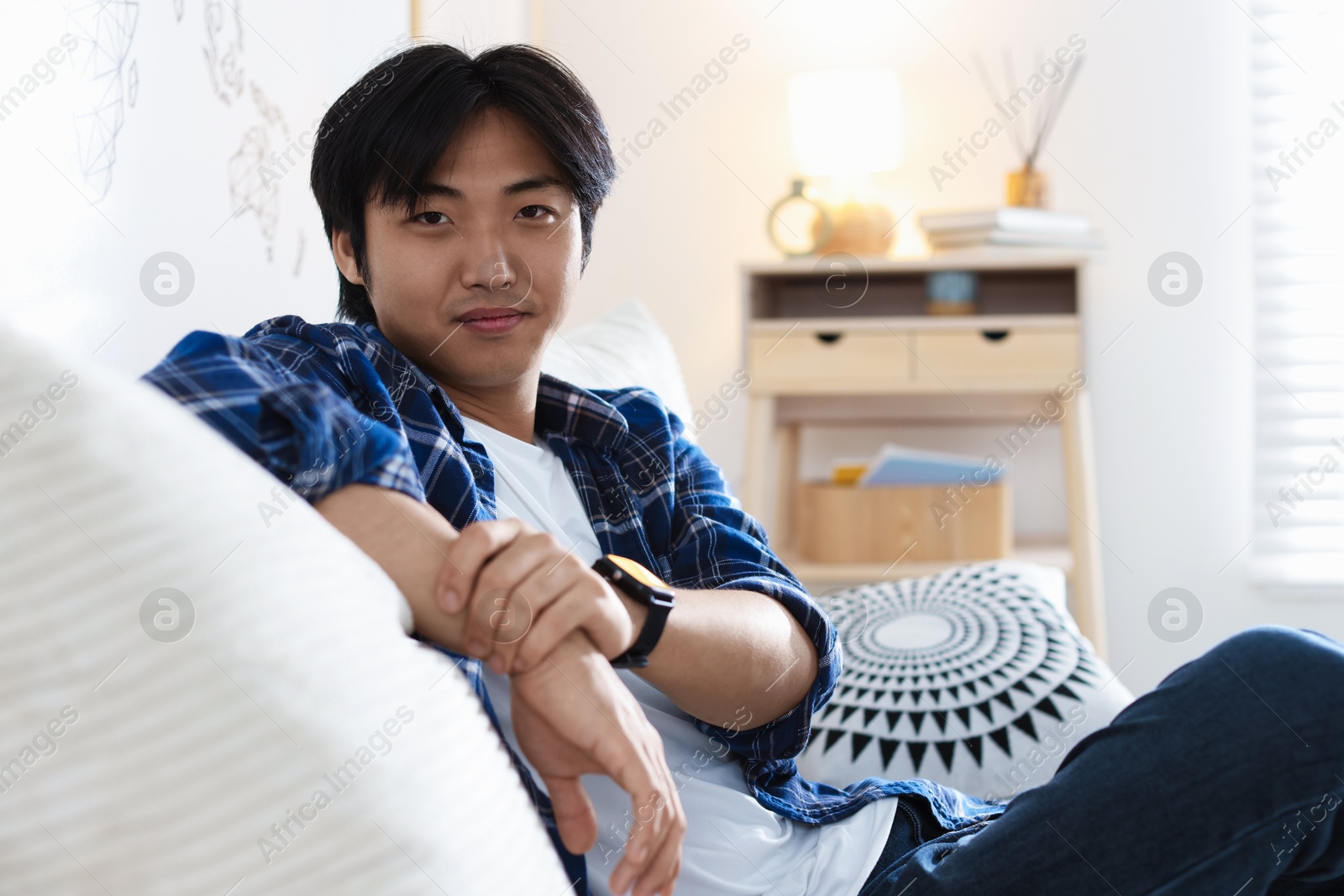 Handsome Asian man sitting on sofa at home Photo of Handsome Asian man sitting on sofa at home