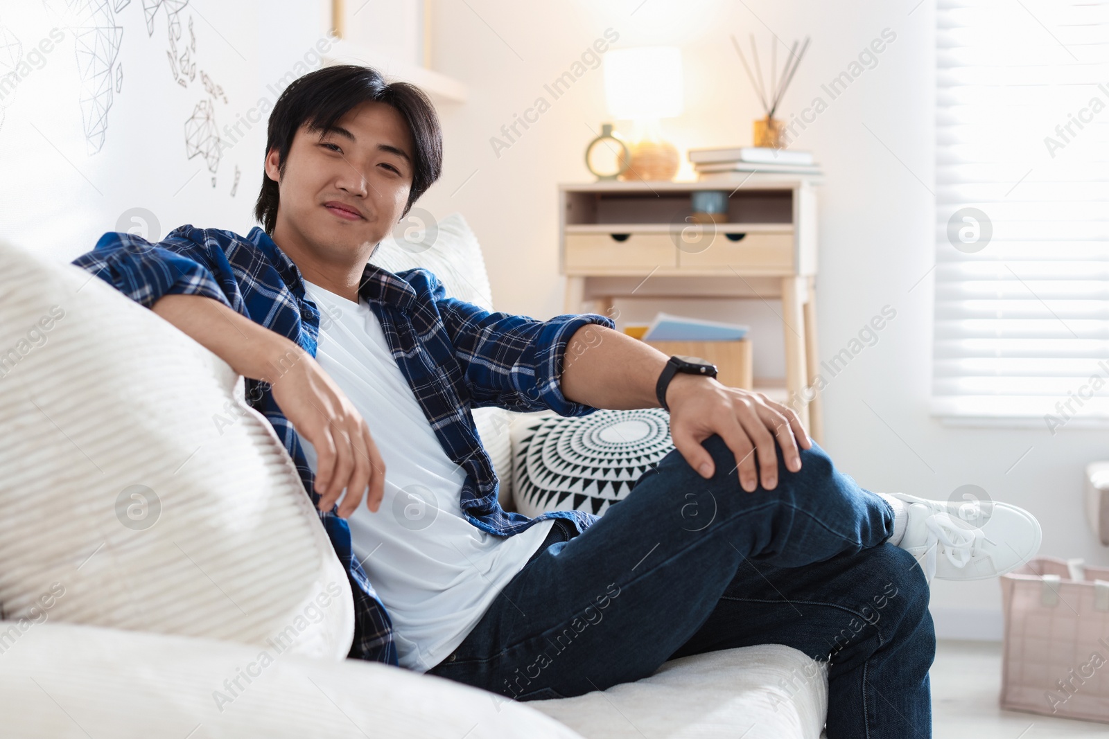 Handsome Asian man sitting on sofa at home Photo of Handsome Asian man sitting on sofa at home