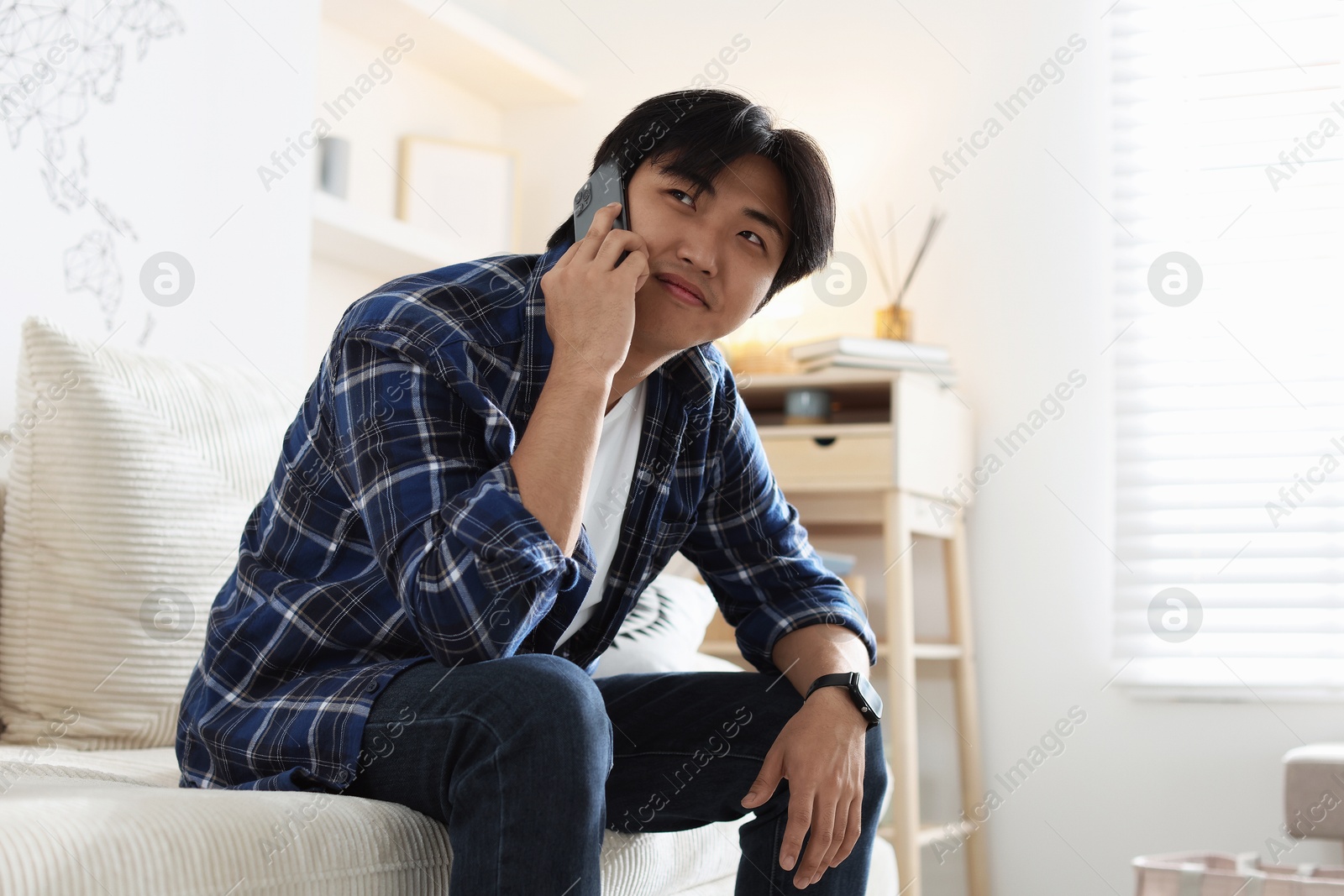 Handsome Asian man talking by smartphone on sofa at home Photo of Handsome Asian man talking by smartphone on sofa at home