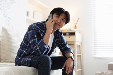 Photo of Handsome Asian man talking by smartphone on sofa at home