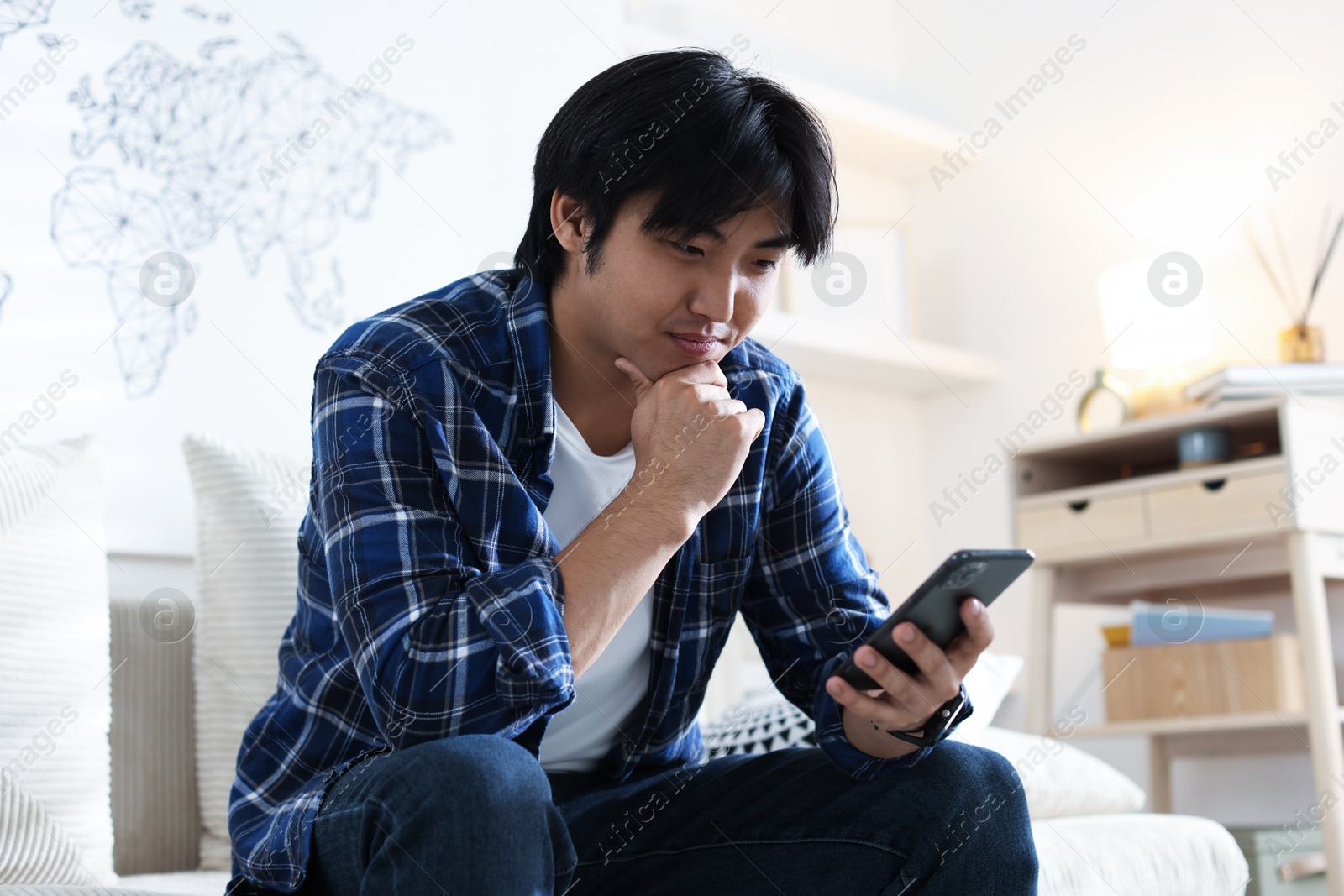 Handsome Asian man with smartphone on sofa at home Photo of Handsome Asian man with smartphone on sofa at home