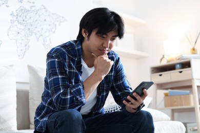 Photo of Handsome Asian man with smartphone on sofa at home