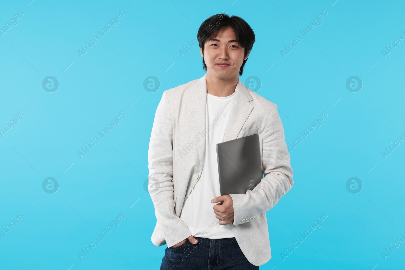 Handsome Asian businessman in suit with laptop on light blue background Photo of Handsome Asian businessman in suit with laptop on light blue background