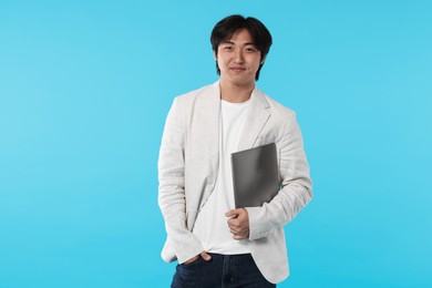 Photo of Handsome Asian businessman in suit with laptop on light blue background