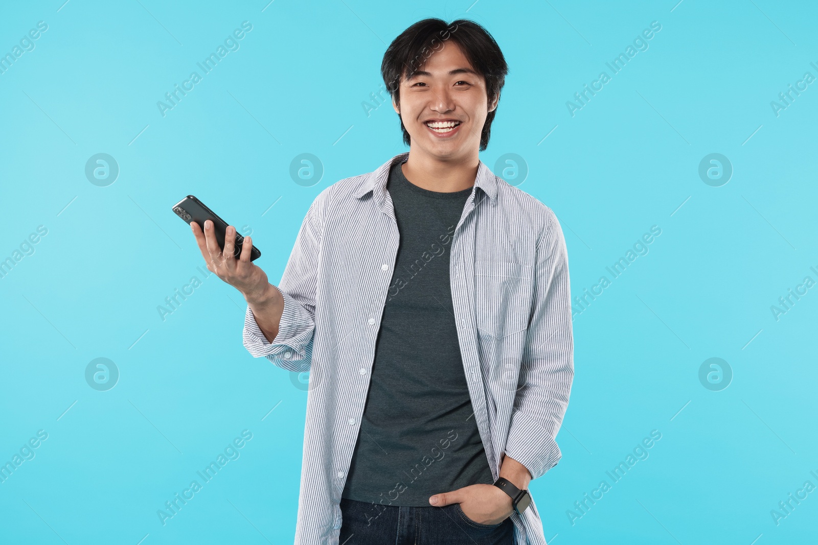 Smiling Asian man with smartphone on light blue background Photo of Smiling Asian man with smartphone on light blue background