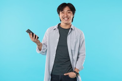 Photo of Smiling Asian man with smartphone on light blue background