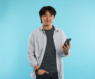 Photo of Handsome Asian man with smartphone on light blue background